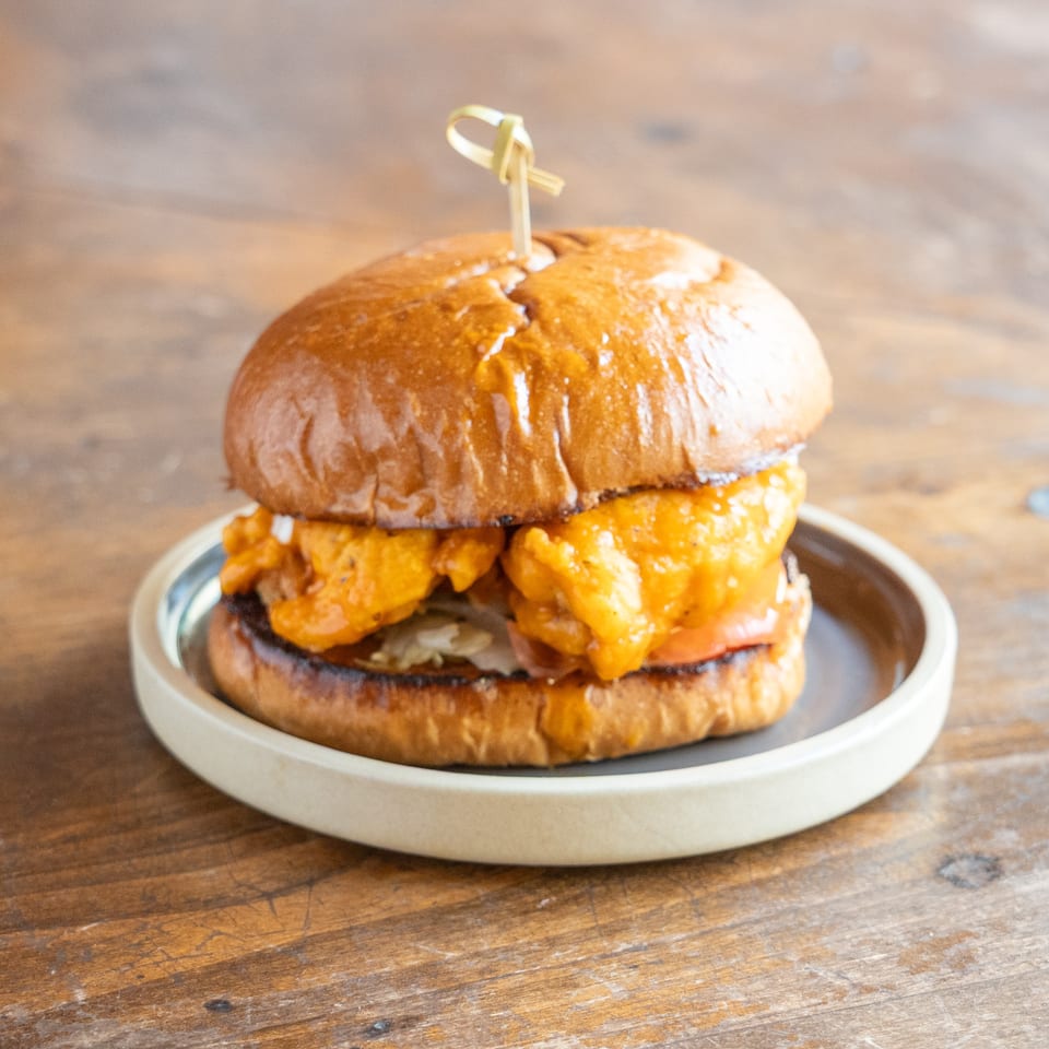 A golden-brown fried chicken sandwich with lettuce and tomato on a plate, on a wooden table.