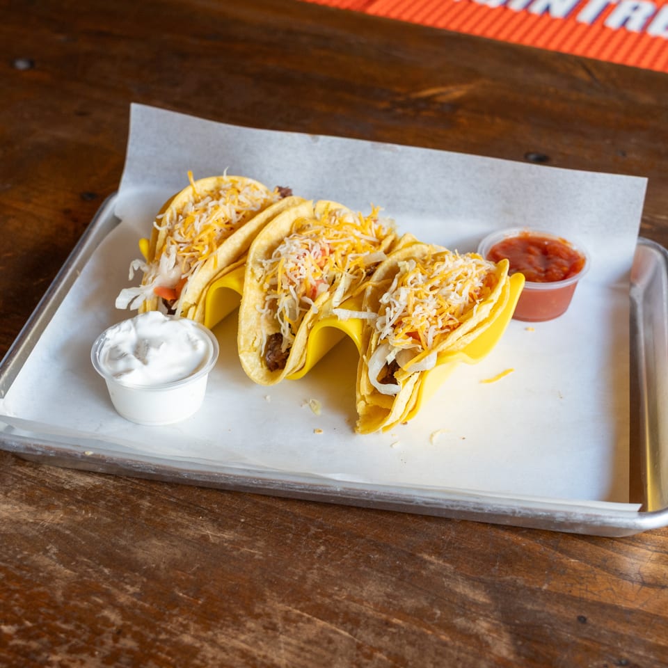 Four hard-shell tacos with meat, cheese, and lettuce, served with salsa and sour cream.