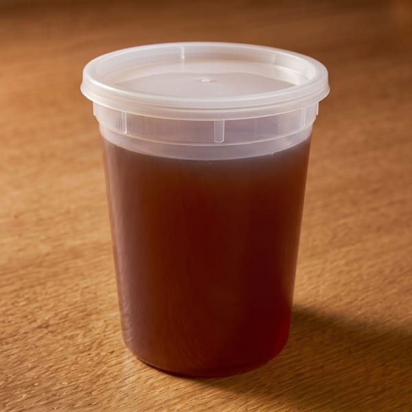 A clear plastic container filled with dark brown liquid, sealed with a translucent lid, on a wooden surface.