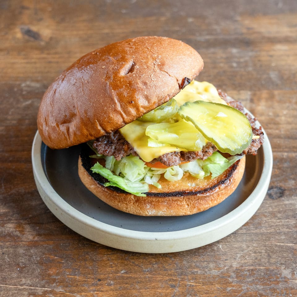 A cheeseburger with lettuce, tomato, and pickles on a toasted bun, served on a gray plate.