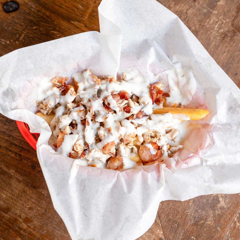 Loaded fries with chicken, bacon, and white sauce in a red basket lined with white paper.